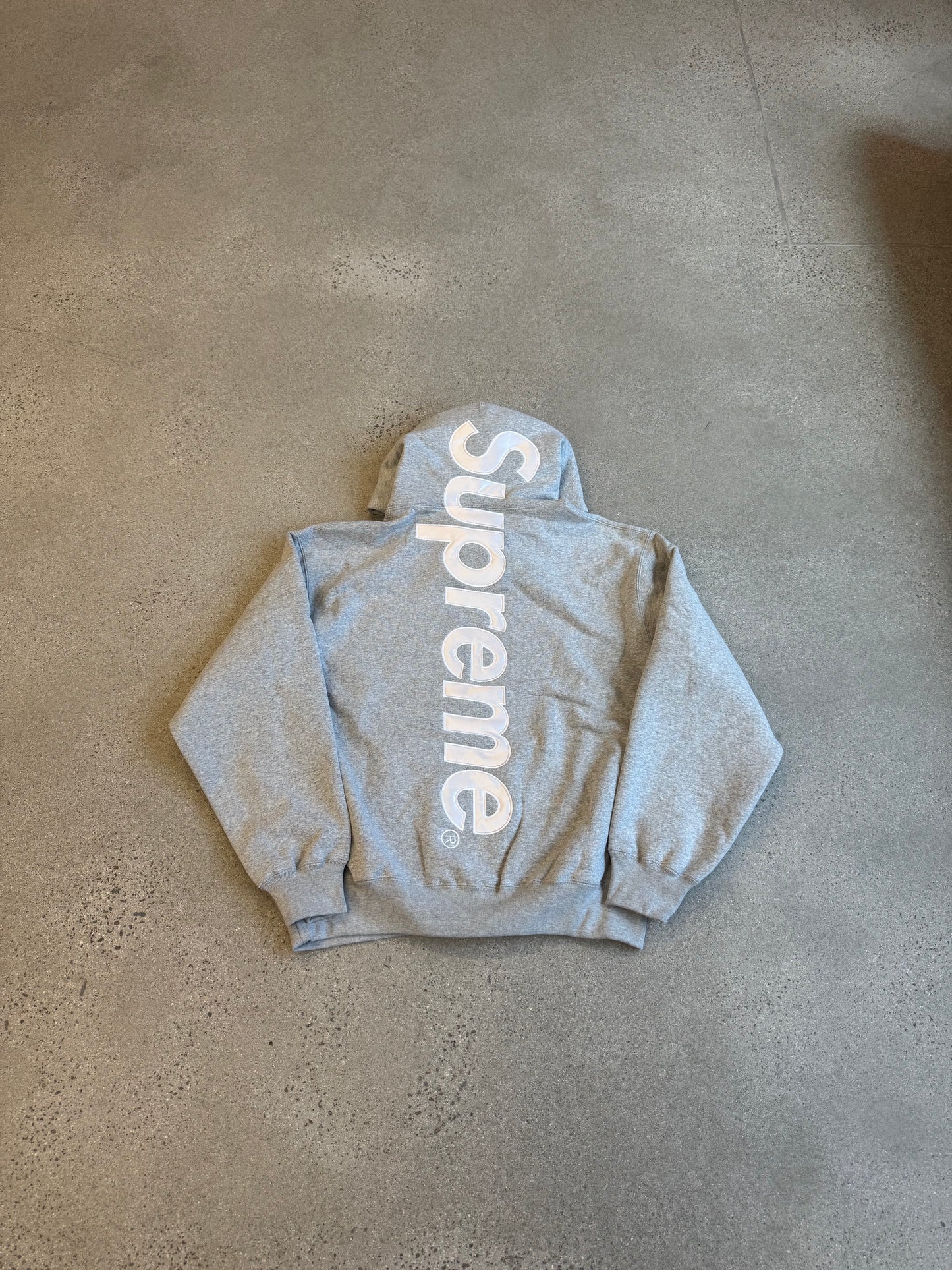 Supreme heather gray hoodie laid flat with large vertical white Supreme satin applique logo across back