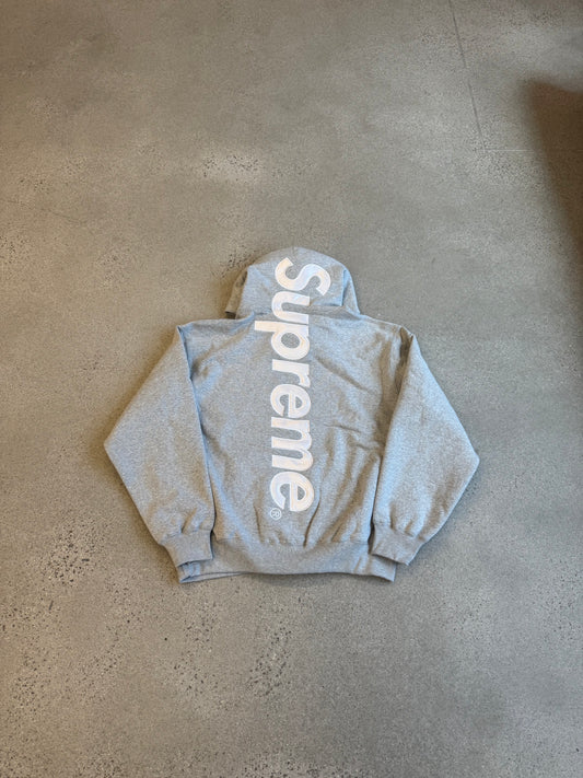 Supreme heather gray hoodie laid flat with large vertical white Supreme satin applique logo across back