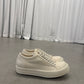 Rick Owens DRKSHDW milk vintage low-top sneakers side angle on concrete floor with curtain backdrop