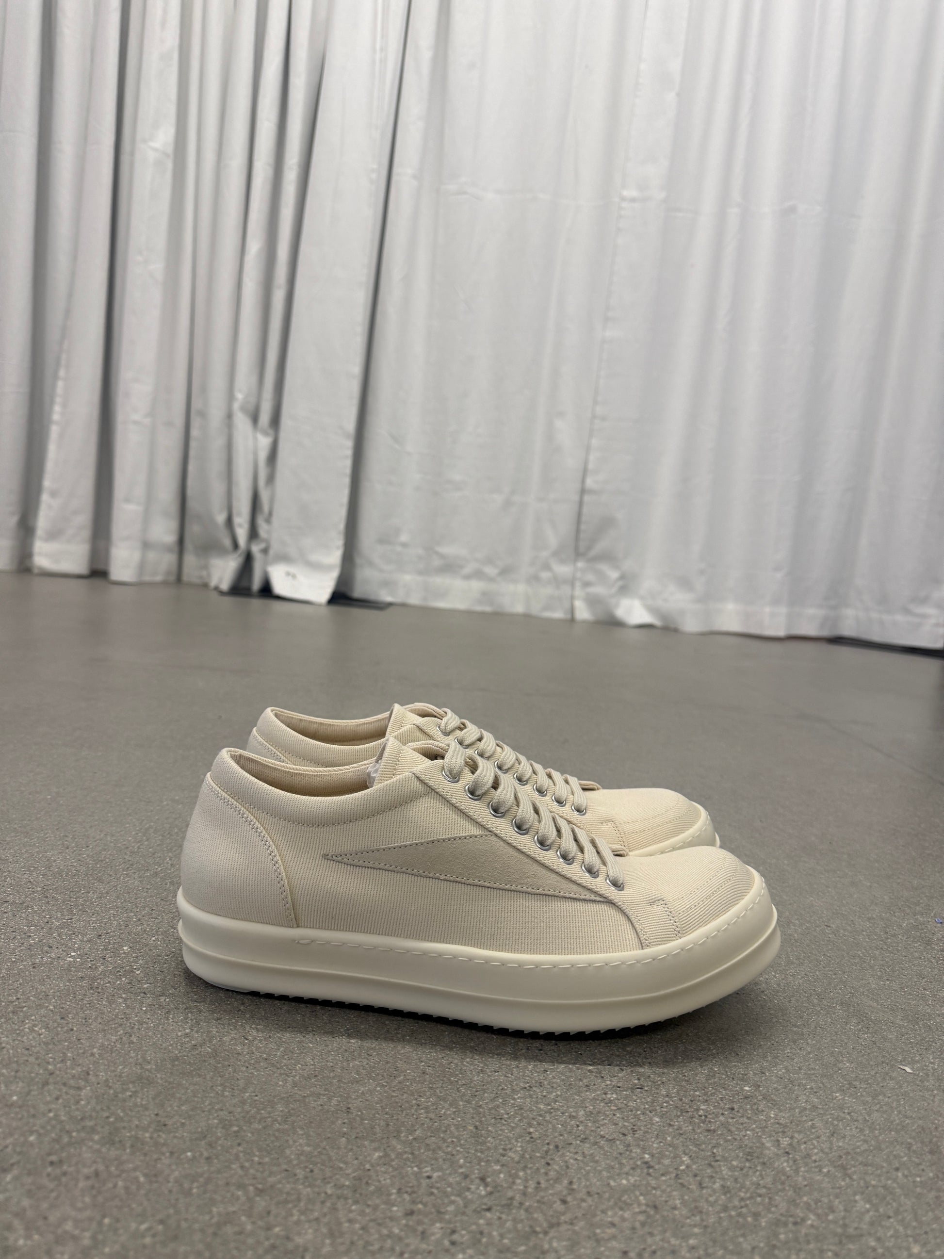Rick Owens DRKSHDW milk vintage low-top sneakers side angle on concrete floor with curtain backdrop