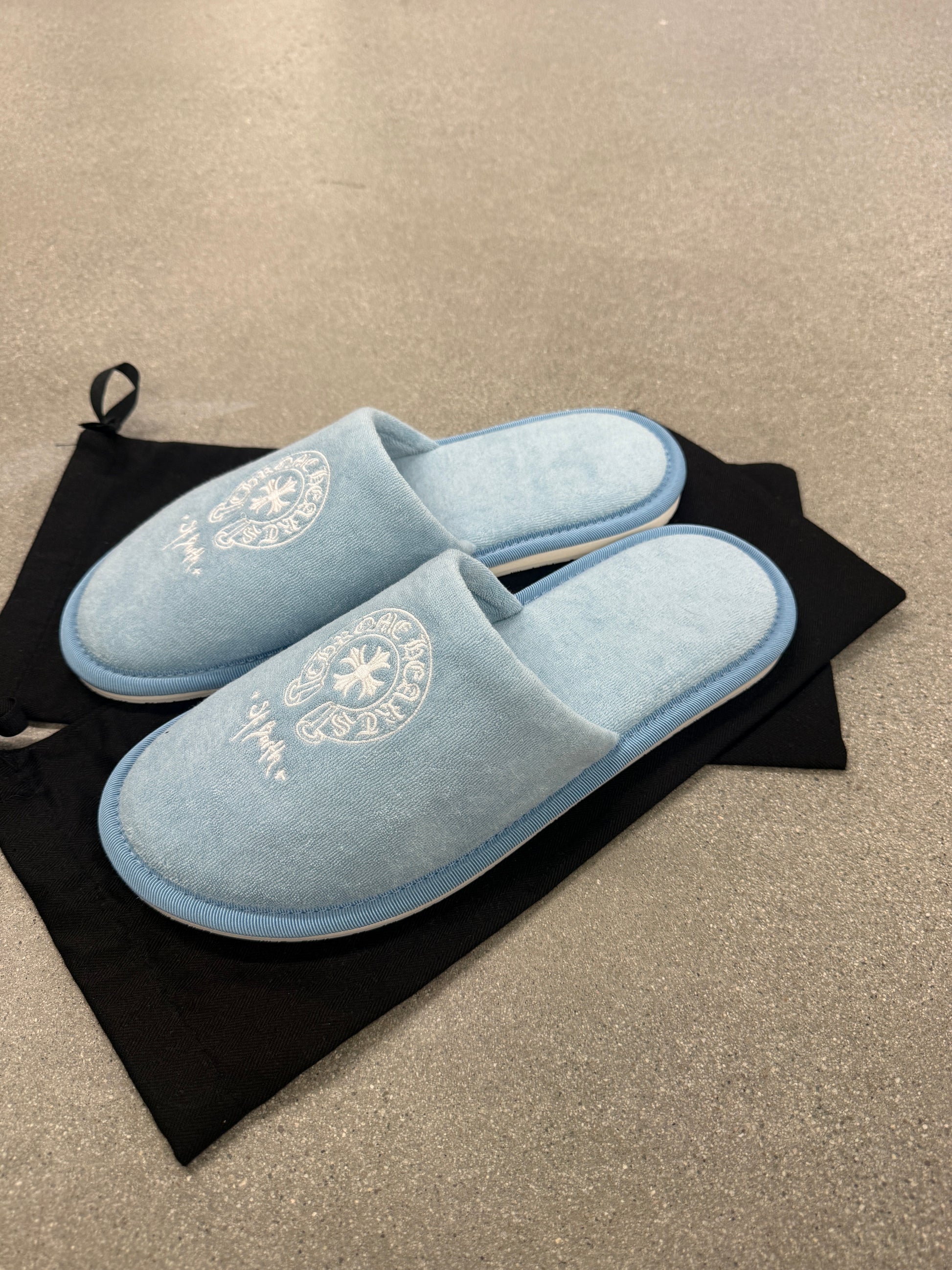 Pair of Chrome Hearts St Barths blue plush slippers displayed on black drawstring dust bag, top view