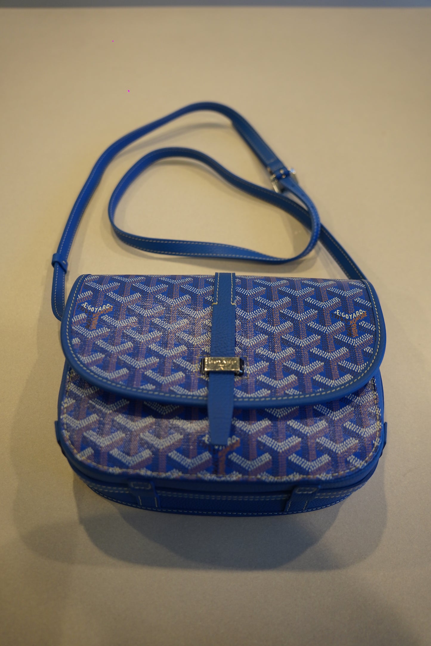Goyard Belvedere PM blue chevron canvas bag close-up of GOYARD engraved name plate and leather strap attach.