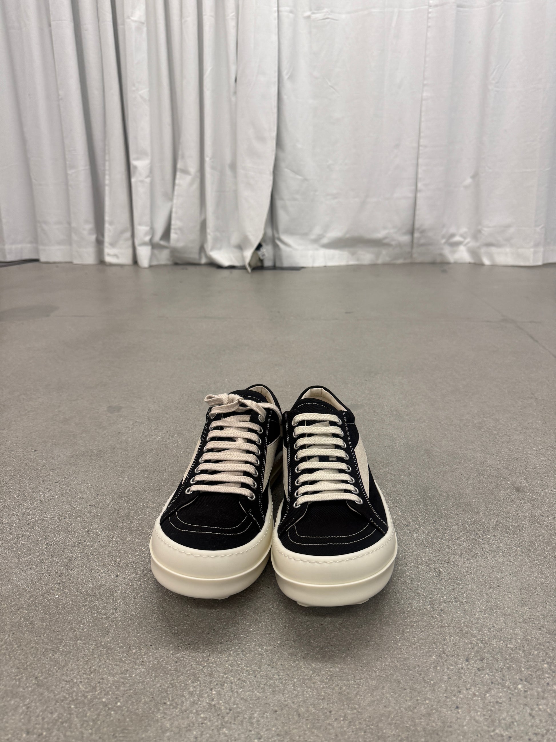 Rick Owens DRKSHDW black Vintage sneakers front view on concrete floor showing white toe cap and waxed laces.