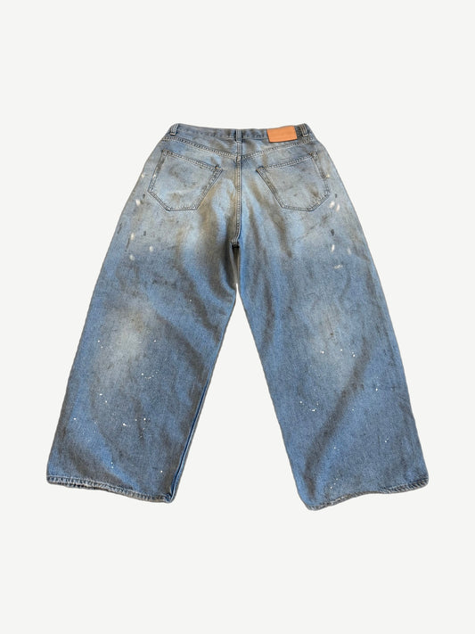 Acne Studios paint splatter loose jeans back, faded wide-leg denim with leather logo patch and distress markings.