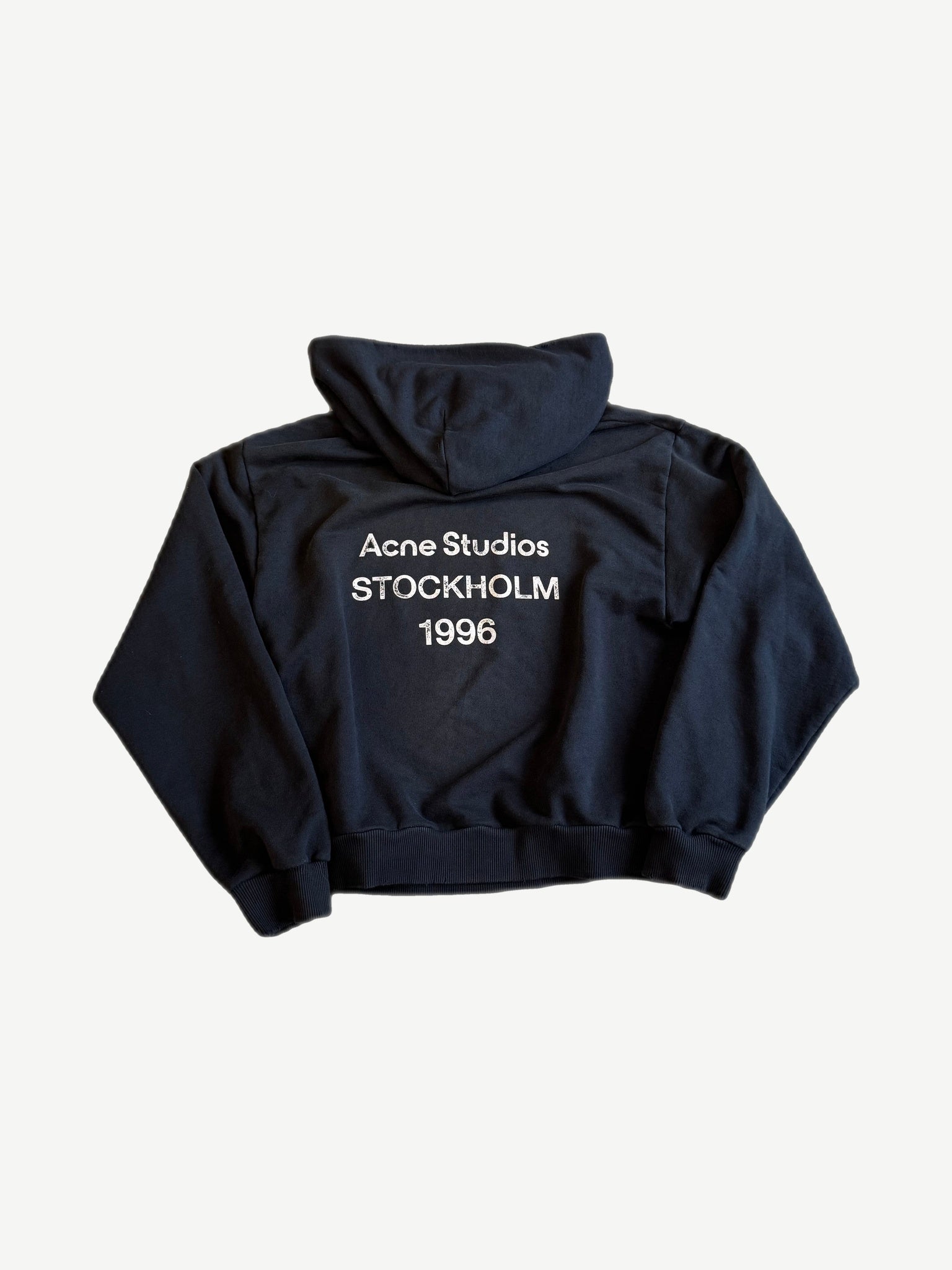 Back of Acne Studios black fleece hoodie with white Acne Studios Stockholm 1996 logo print.