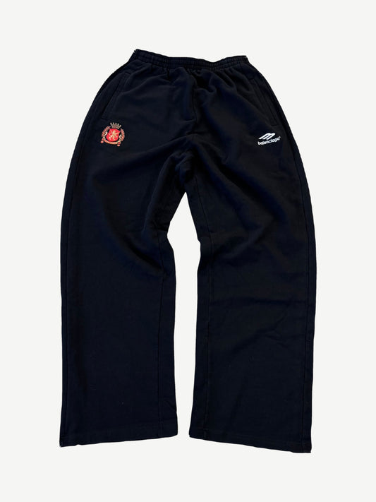 Balenciaga black soccer crest sweatpants with embroidered heraldic lion shield and sportswear wing logo on thighs.