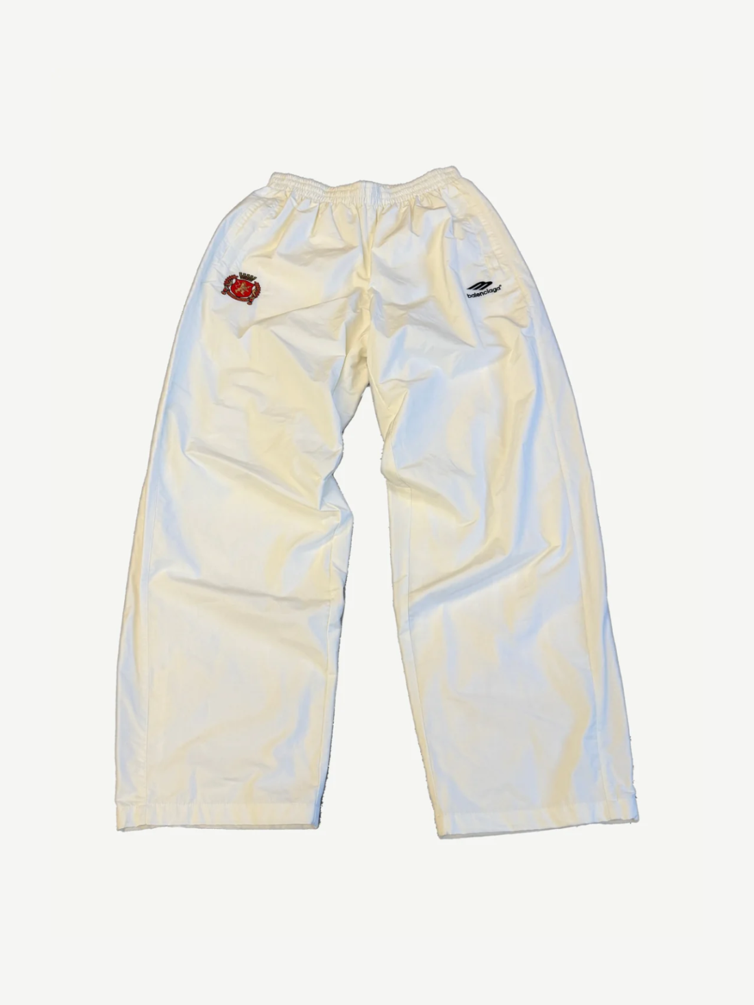Balenciaga white cotton track pants front with embroidered soccer crest patch and elastic waistband.