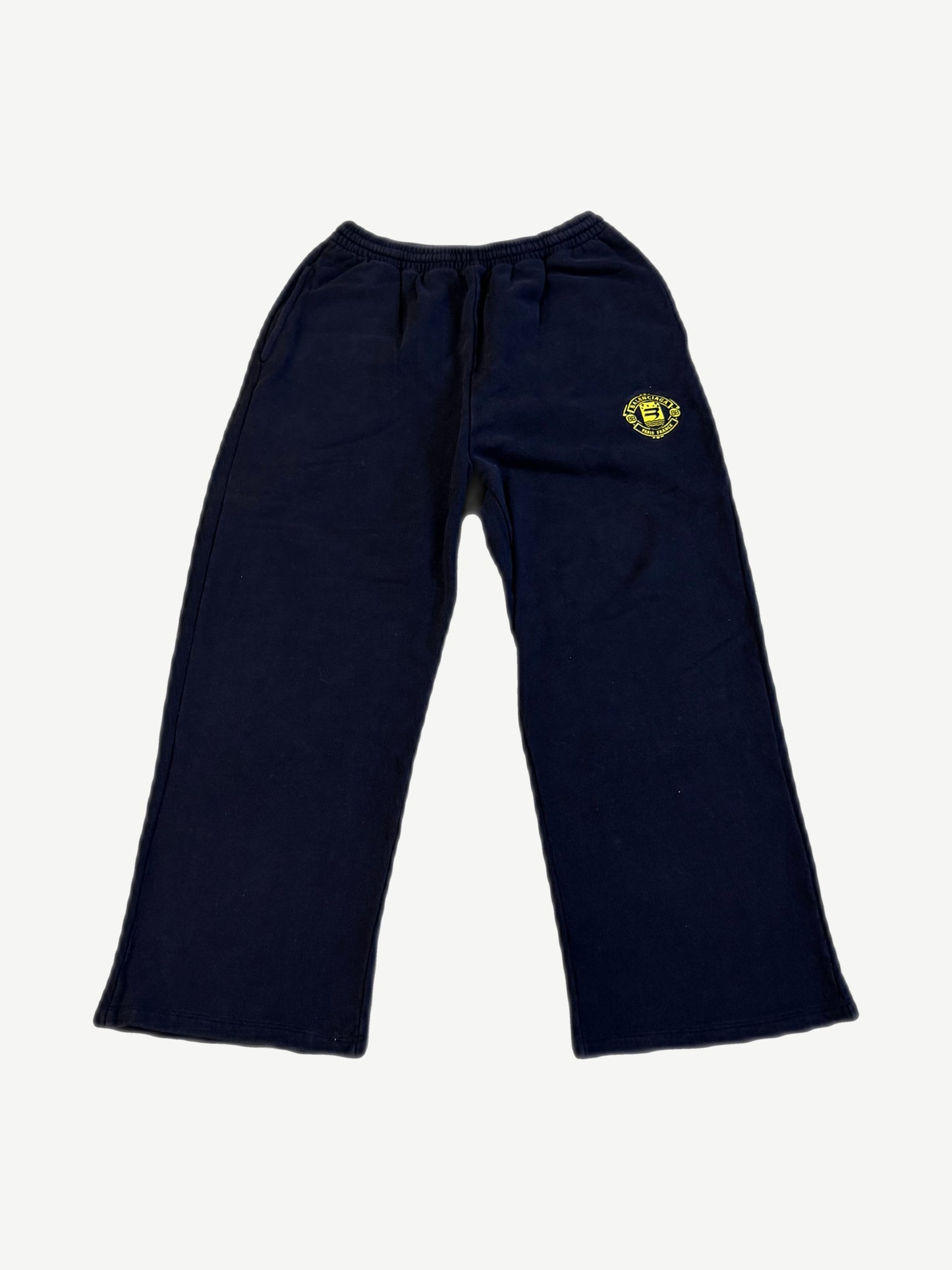 Balenciaga navy sweatpants with yellow circular Paris France crest logo on thigh and relaxed straight-leg fit.