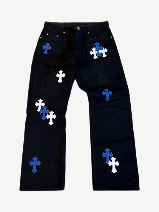 Chrome Hearts black jeans front, scattered blue and white leather cross patches with fleur knee dagger appliques.