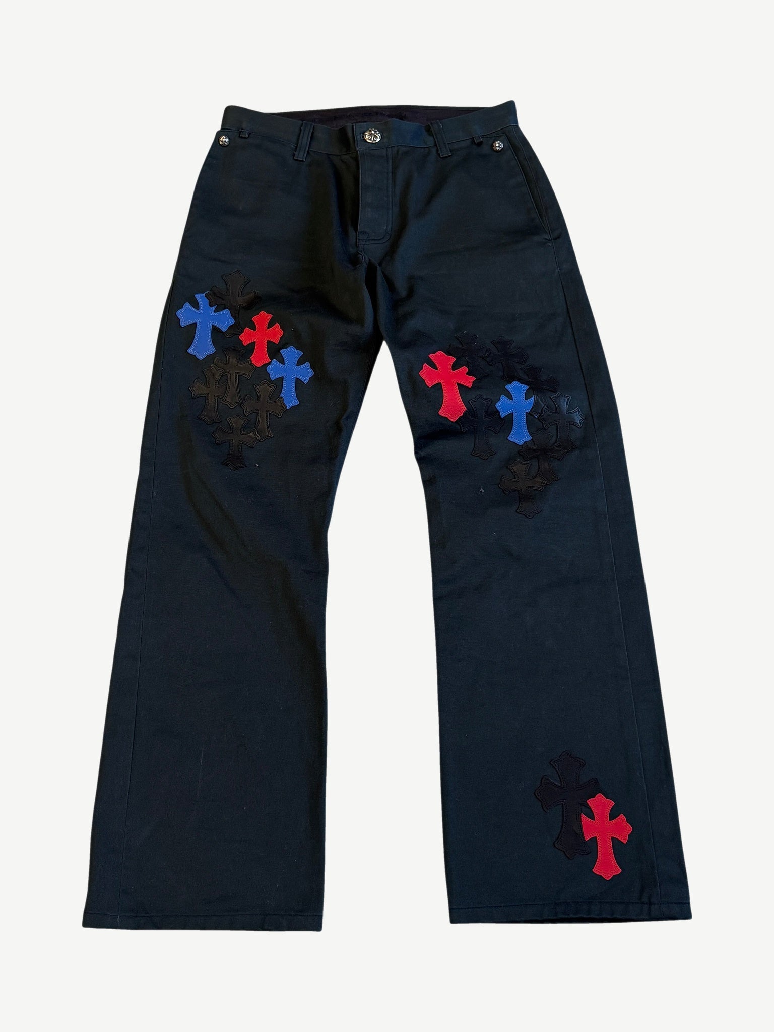 Chrome Hearts black chino pants front covered in stitched black, red and blue leather cross patches at thighs.