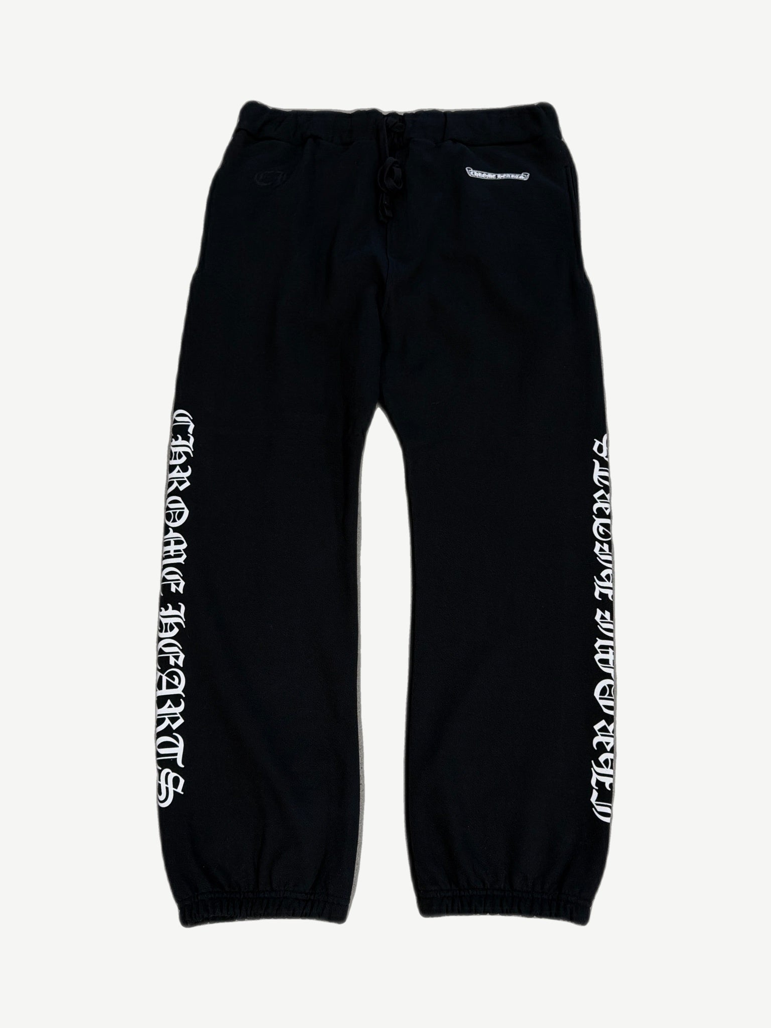 Chrome Hearts black sweatpants front, white Old English scroll logo down both legs with drawstring waist.