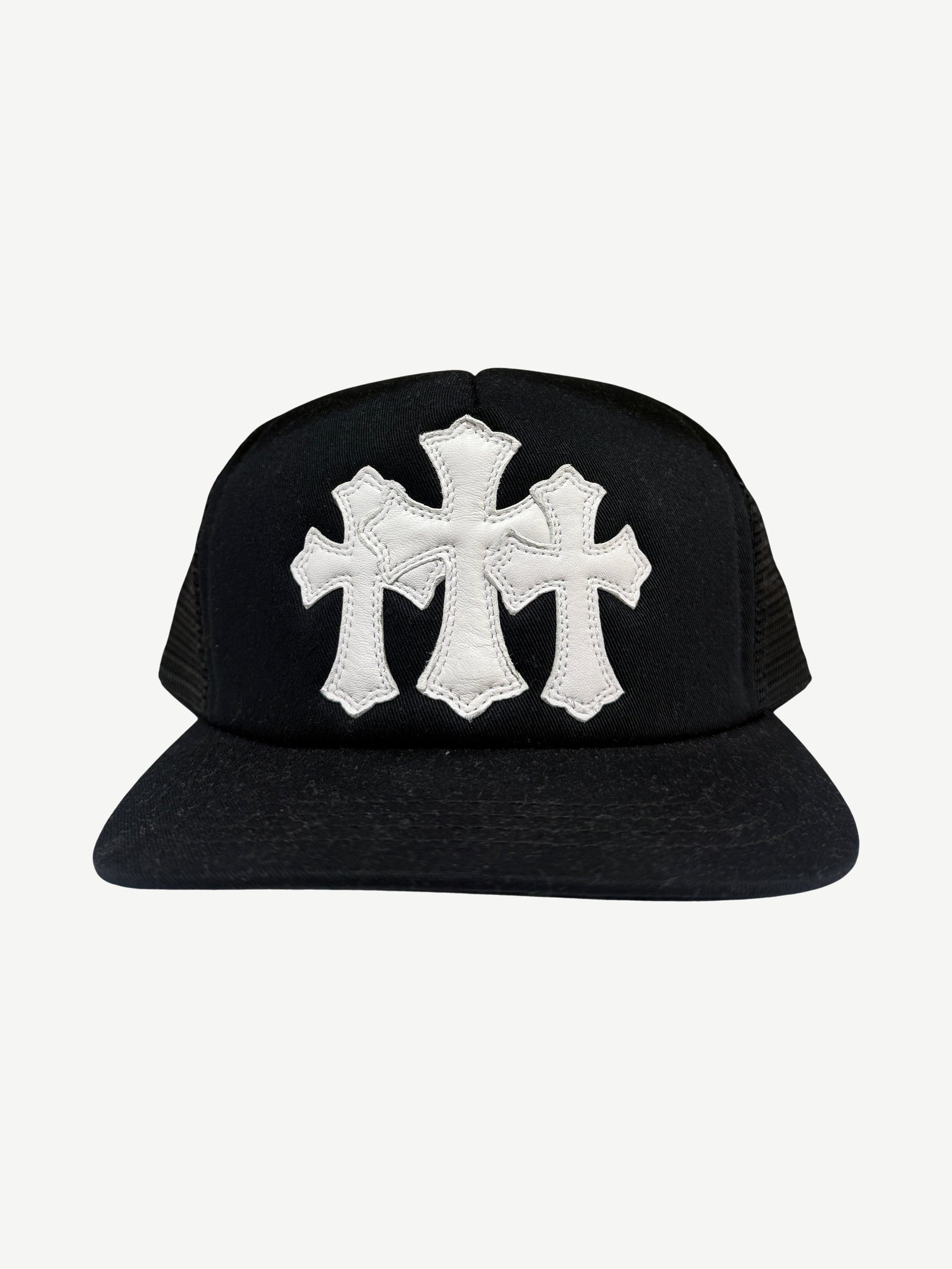 Chrome Hearts black trucker hat front with three white leather cross patches stitched across the crown panels.