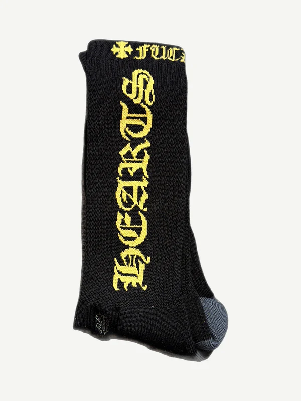 Chrome Hearts black crew socks with vertical yellow Old English Chrome Hearts script and cross logo.