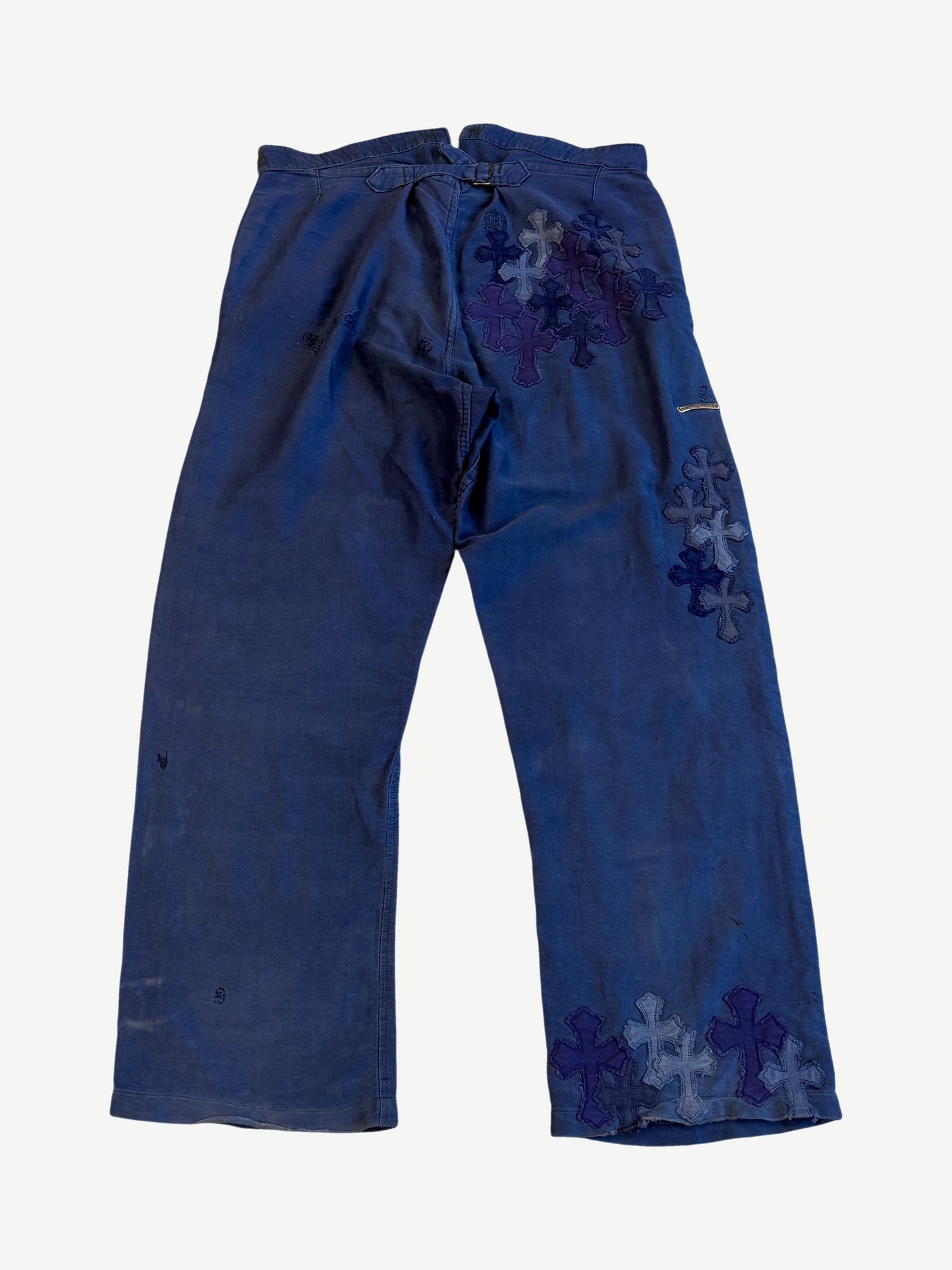 Chrome Hearts blue French work pants back, clustered cross leather patches across right hip and lower leg.