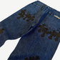 Chrome Hearts cross patch jeans detail, close-up of black leather cross patches on dark indigo denim