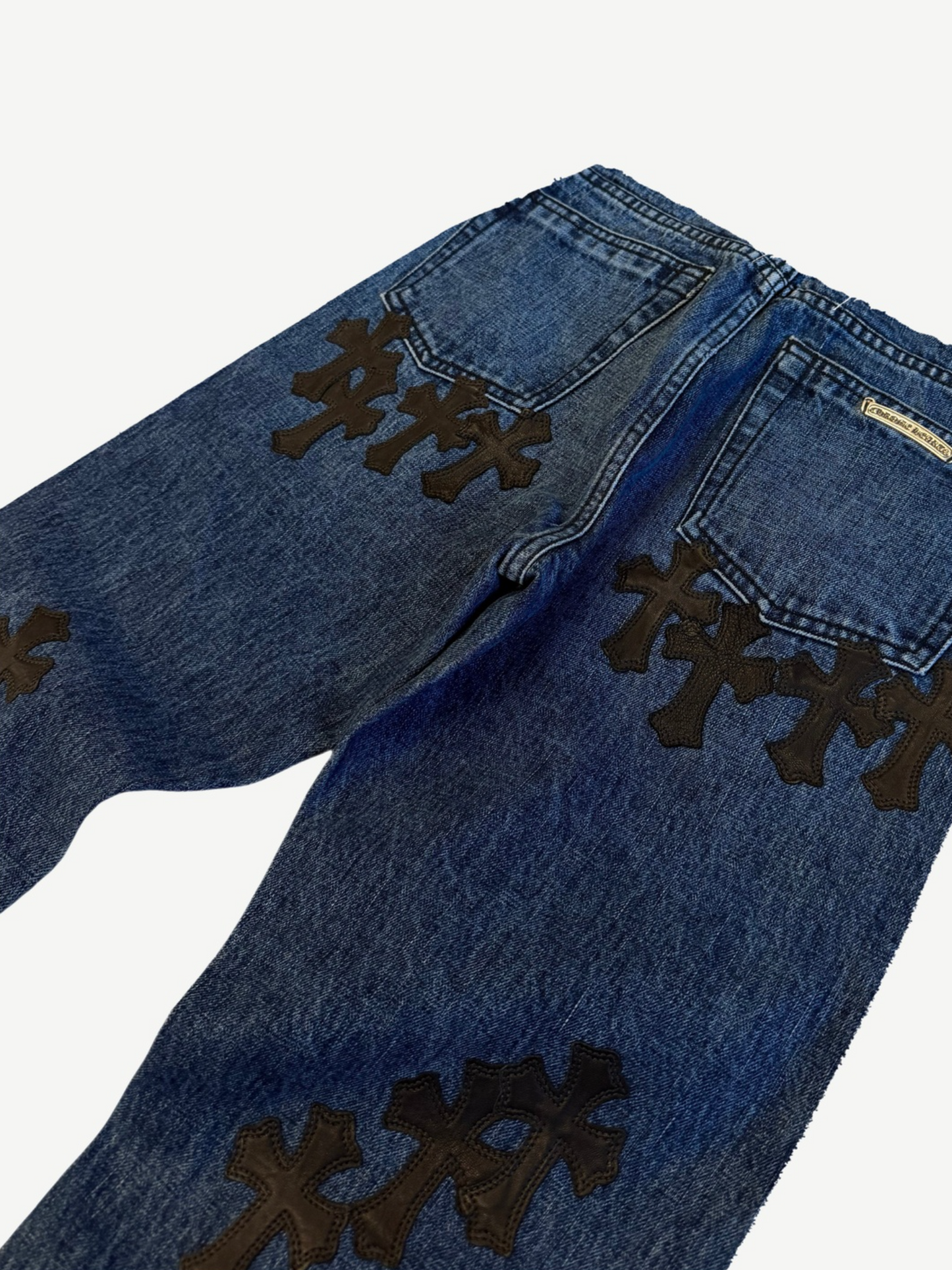 Chrome Hearts cross patch jeans detail, close-up of black leather cross patches on dark indigo denim