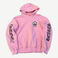 Chrome Hearts Matty Boy pink hoodie front with checker smiley chest patch and gothic Hearts sleeve lettering.