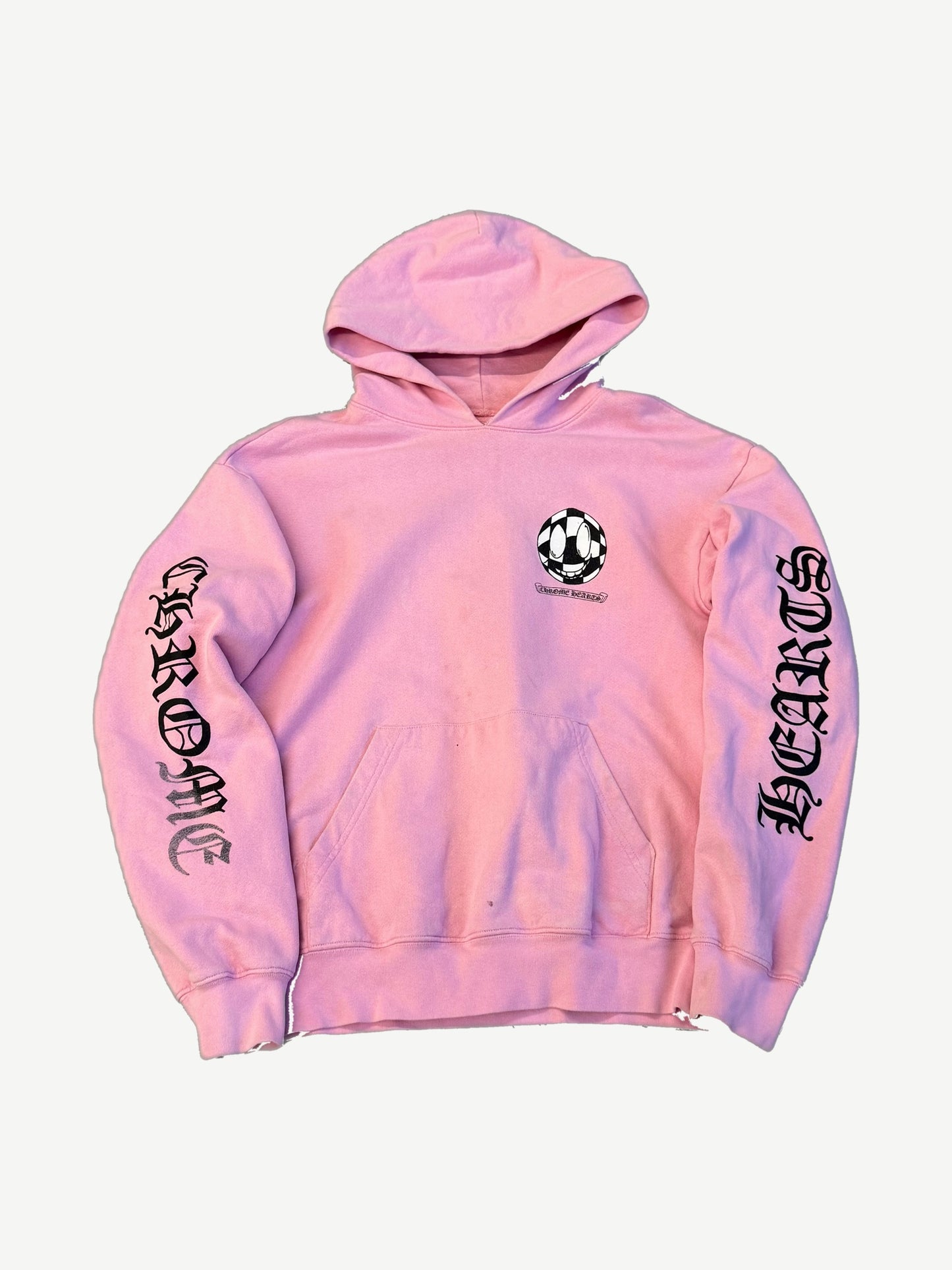 Chrome Hearts Matty Boy pink hoodie front with checker smiley chest patch and gothic Hearts sleeve lettering.