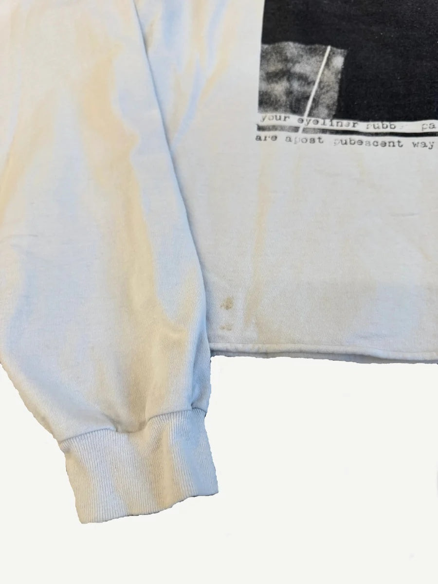 ERD off-white longsleeve close-up of left cuff and lower hem showing ribbed cuff and typewriter text fragments.