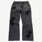 HMDD gray washed denim pants front with scattered tonal black HMDD monogram patches stitched across both legs.