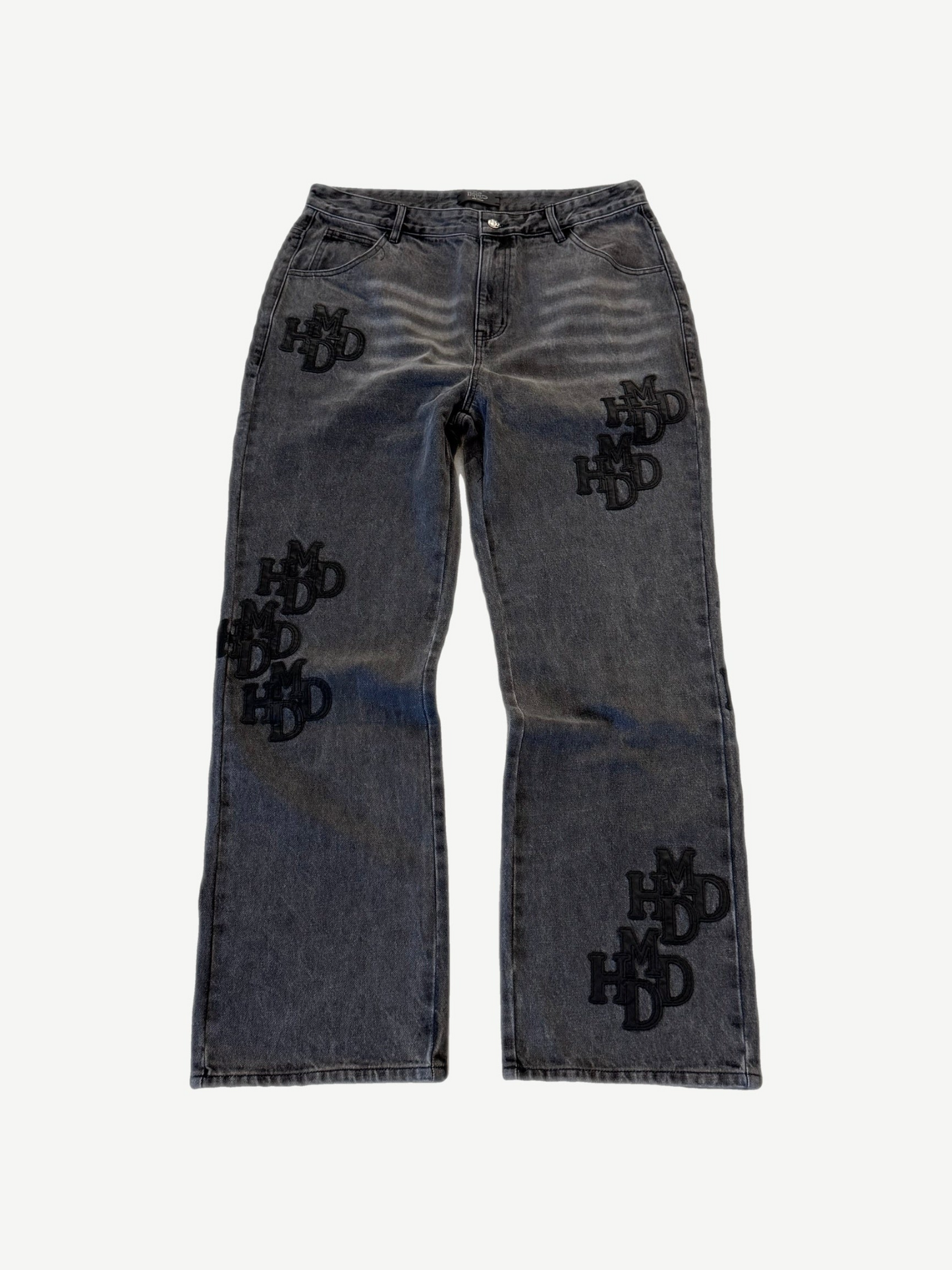 HMDD gray washed denim pants front with scattered tonal black HMDD monogram patches stitched across both legs.