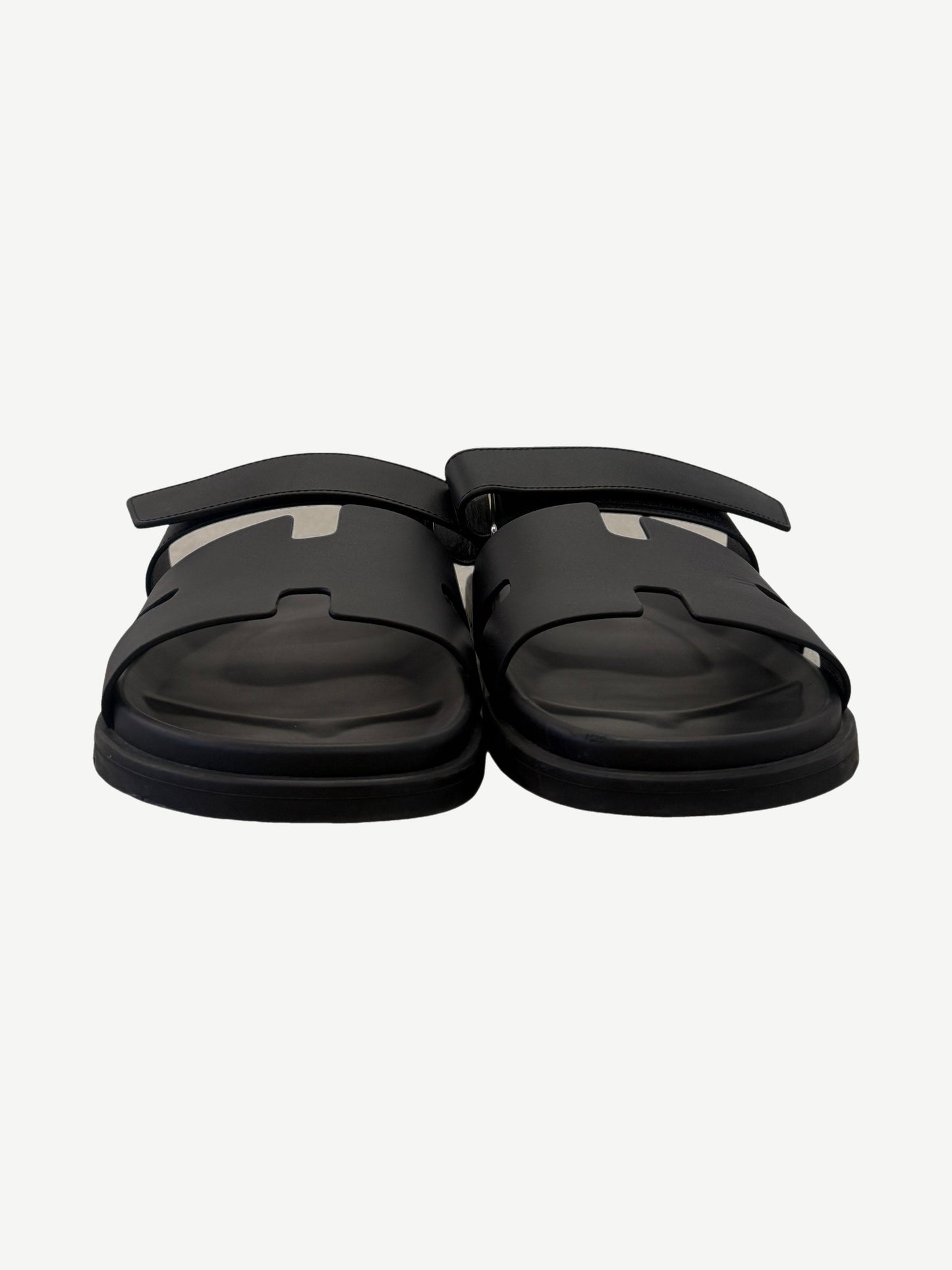 Hermes Chypre sandal pair front view in noir black calfskin, showing H-cutout vamp and adjustable ankle strap.