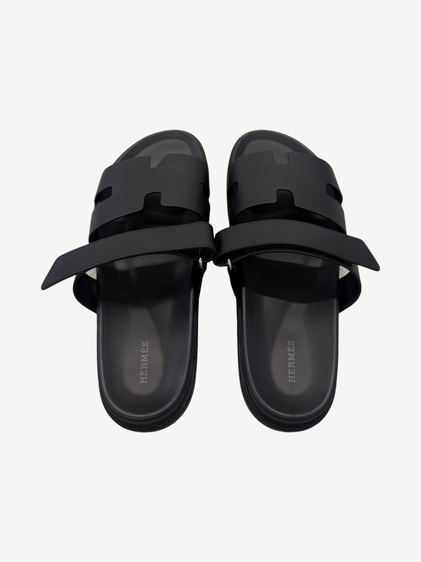 Hermes Chypre sandal pair top-down view, black calfskin straps unfastened revealing Hermes branded leather insoles.