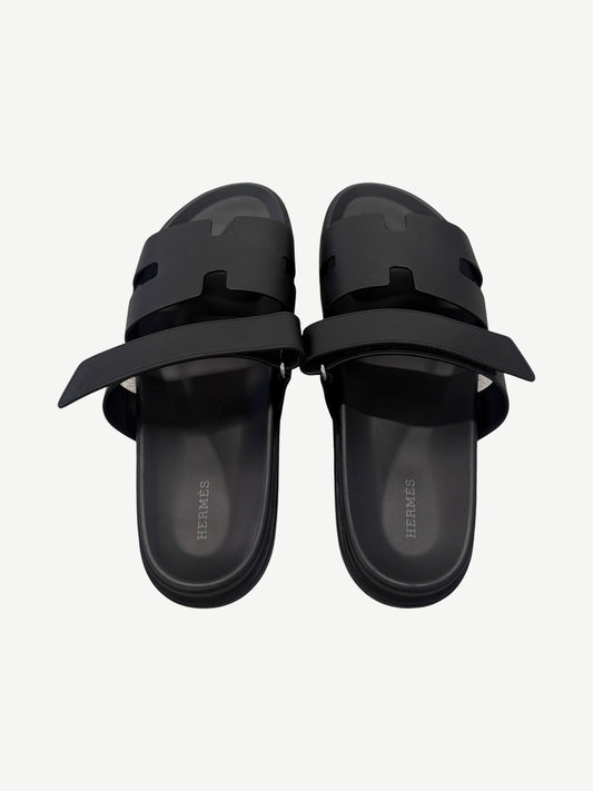 Hermes Chypre sandal pair top-down view, black calfskin straps unfastened revealing Hermes branded leather insoles.