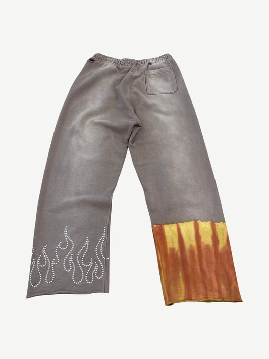 Paly Mass sweatpants back view in faded gray brown with orange tie-dye hem panel and rhinestone flame motif