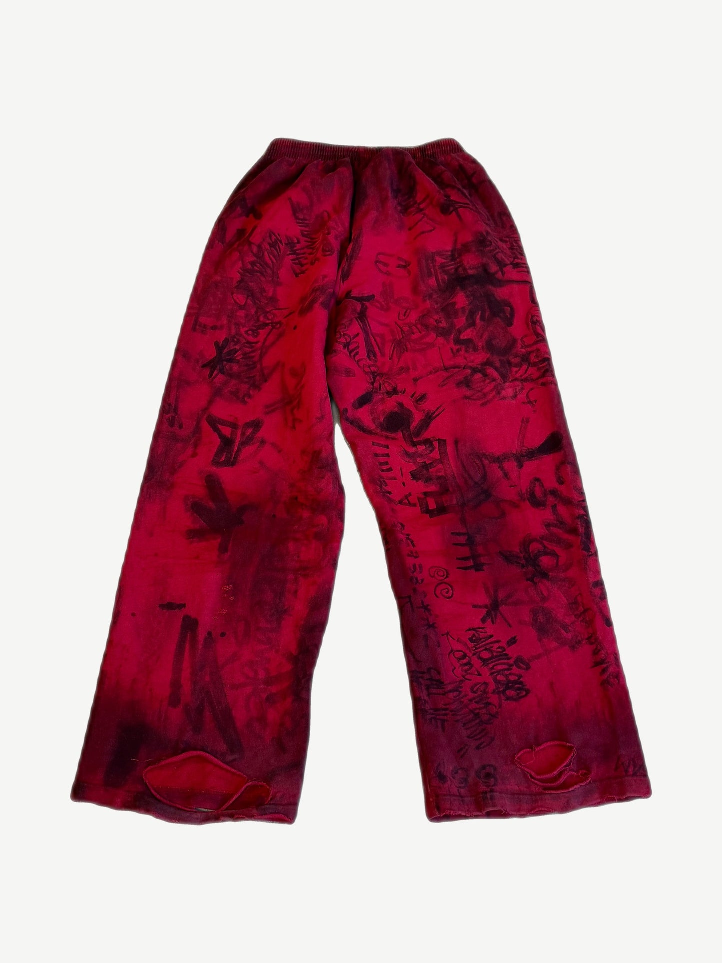 Balenciaga red baggy sweatpants back view with allover black graffiti tag print and distressed holes near hems.