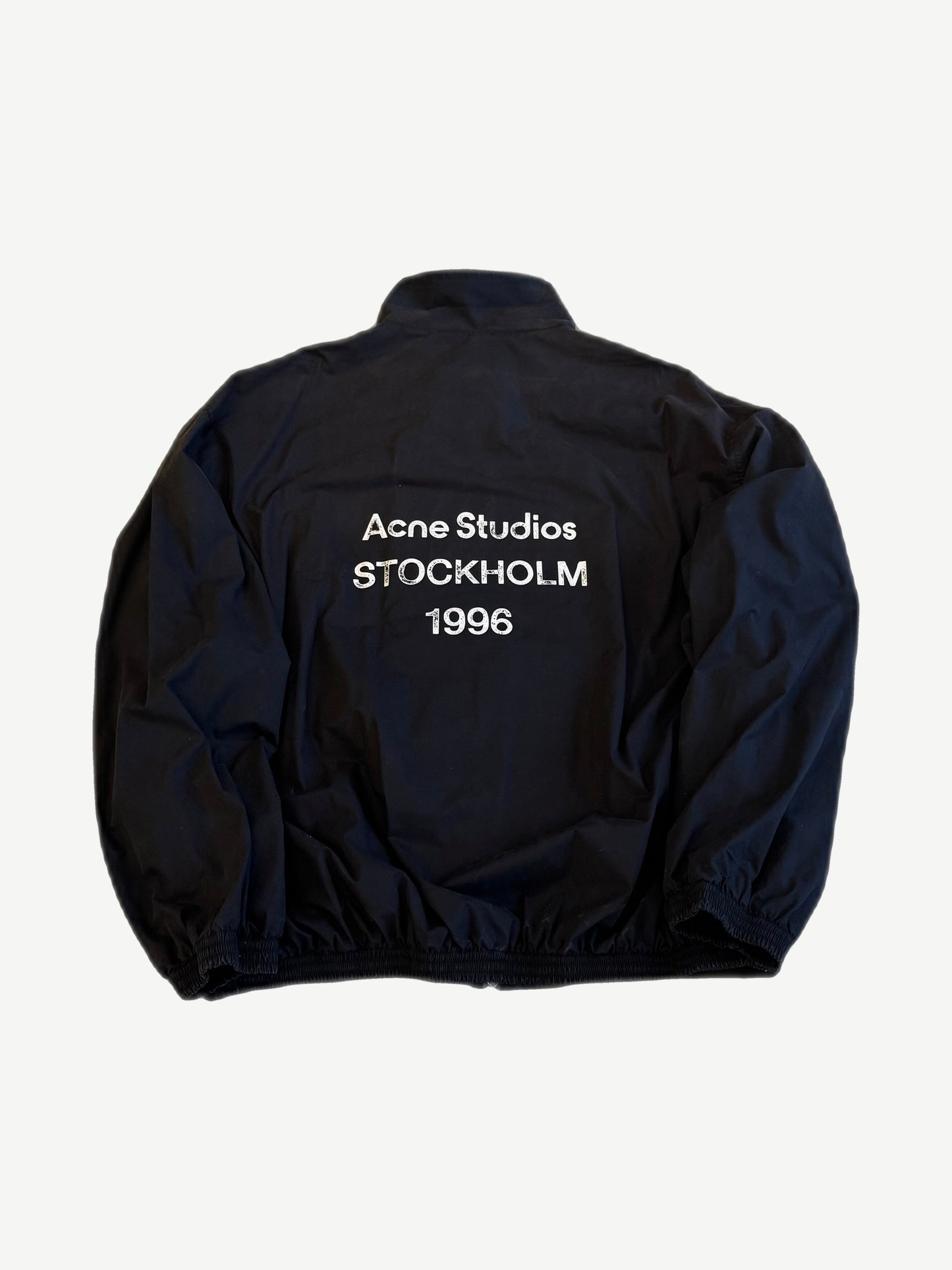 Back of Acne Studios navy nylon jacket with washed white Acne Studios Stockholm 1996 logo print