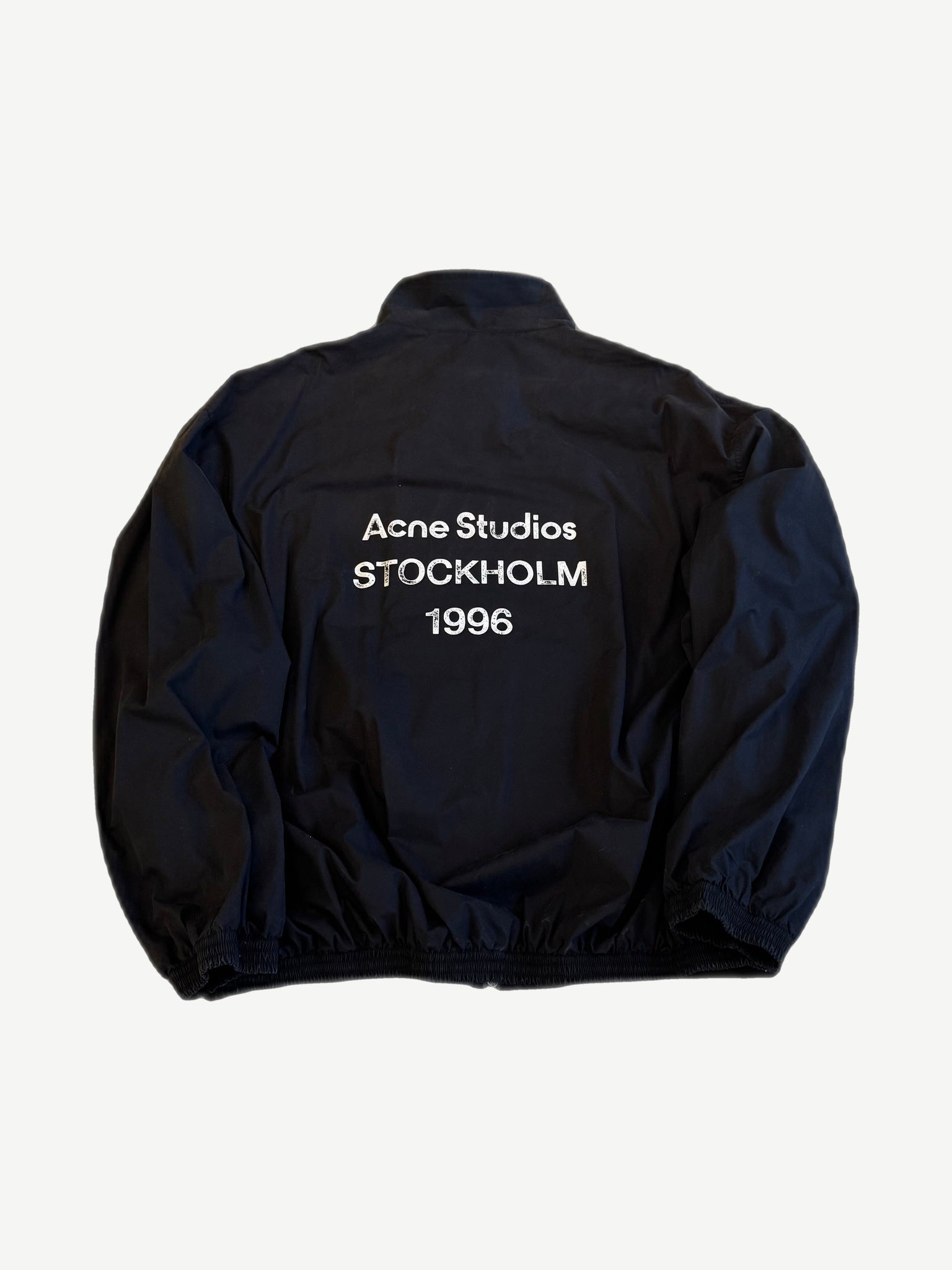 Back of Acne Studios navy nylon jacket with washed white Acne Studios Stockholm 1996 logo print