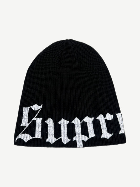 Supreme black ribbed knit beanie with large white Old English script logo wrapping the lower cuff