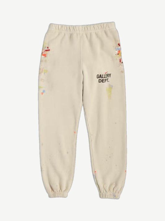 Gallery Dept cream sweatpants front view with black logo center thigh and multicolor paint splatter detailing