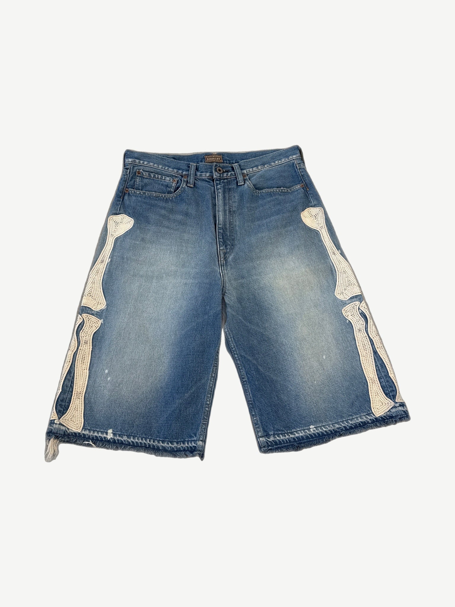 Kapital blue denim jorts front, mid-wash with embroidered cream bone appliques running down both leg sides.
