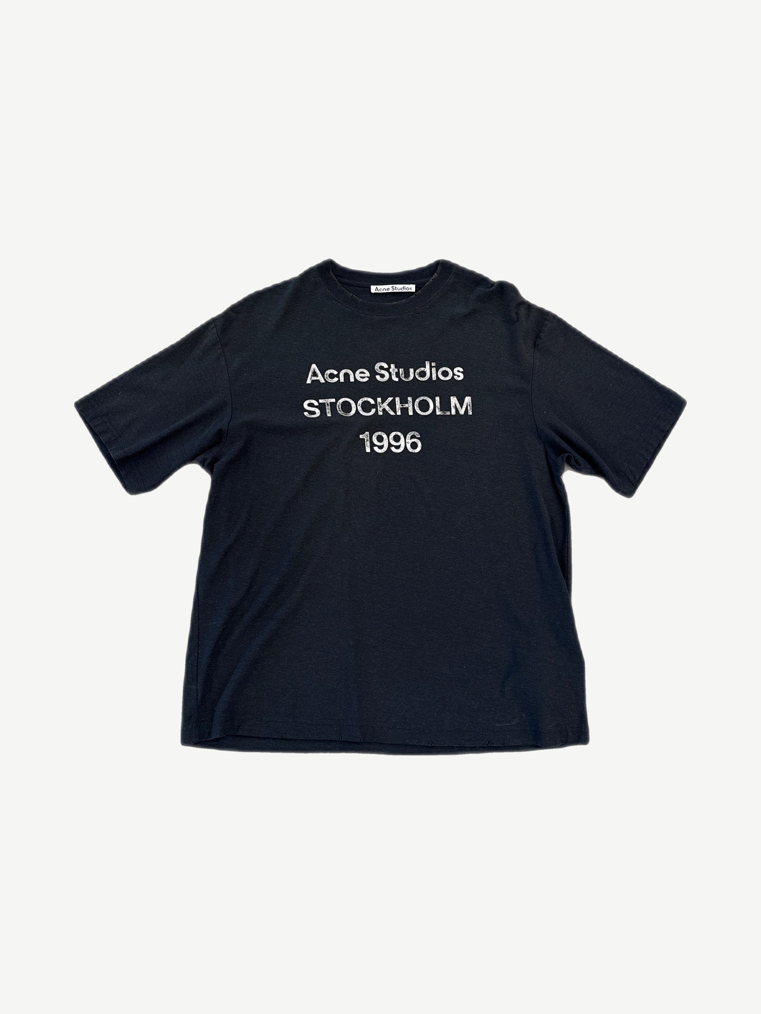 Acne Studios black tee with white Stockholm 1996 distressed logo print centered on chest, front view.
