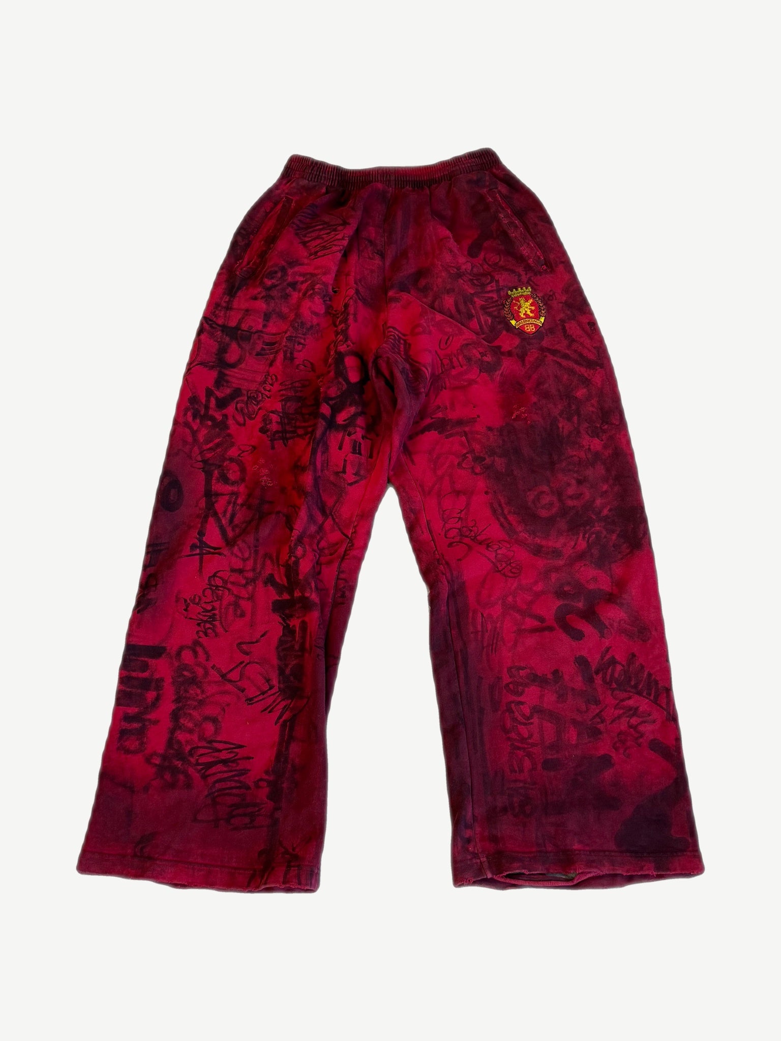 Balenciaga red baggy sweatpants front with allover black graffiti print and embroidered gold lion crest on right hip.
