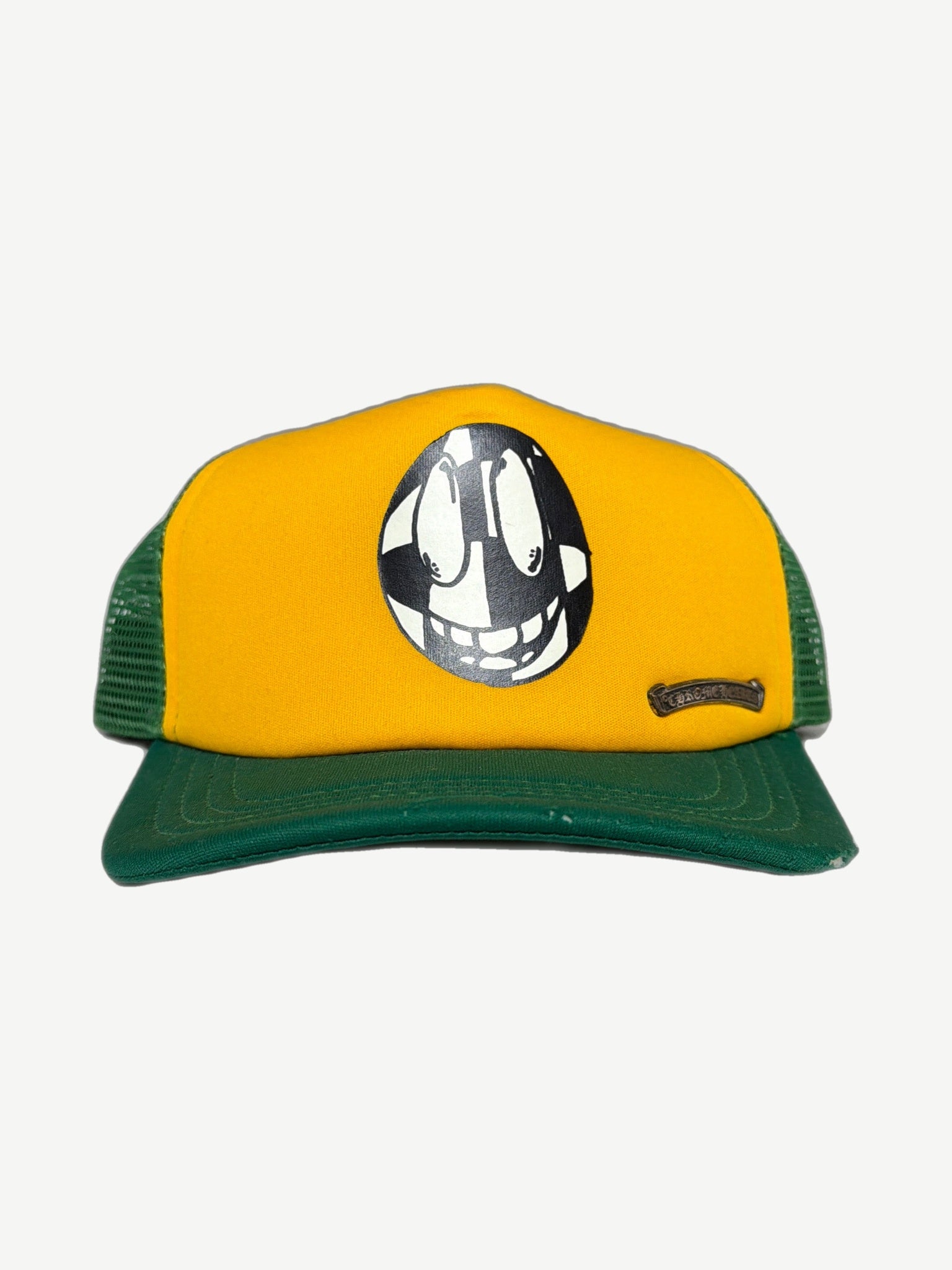 Chrome Hearts Matty Boy yellow and green trucker hat with 99 Eyes cartoon face print and metal logo plaque