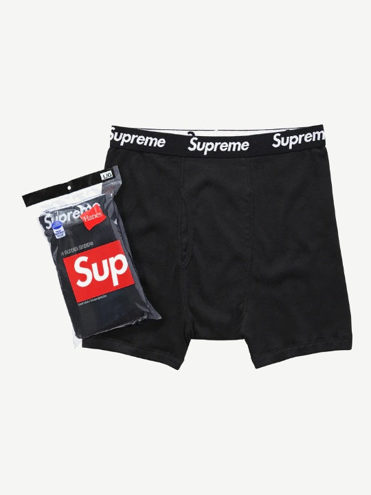 Supreme x Hanes black boxer briefs with white Supreme logo waistband shown next to sealed red box logo pack.