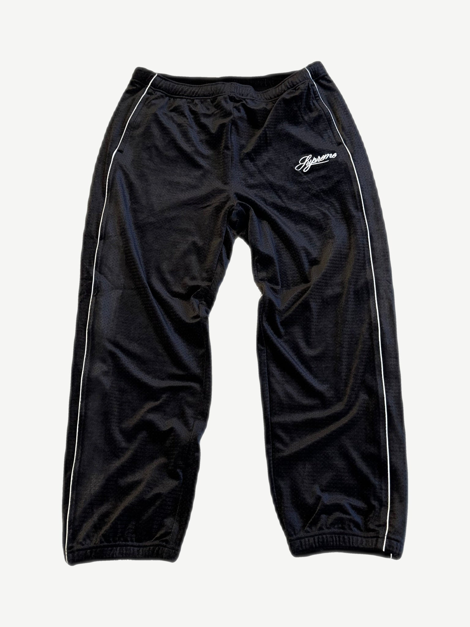Supreme black velour mesh track pants with white piping side stripes and script Supreme thigh logo.