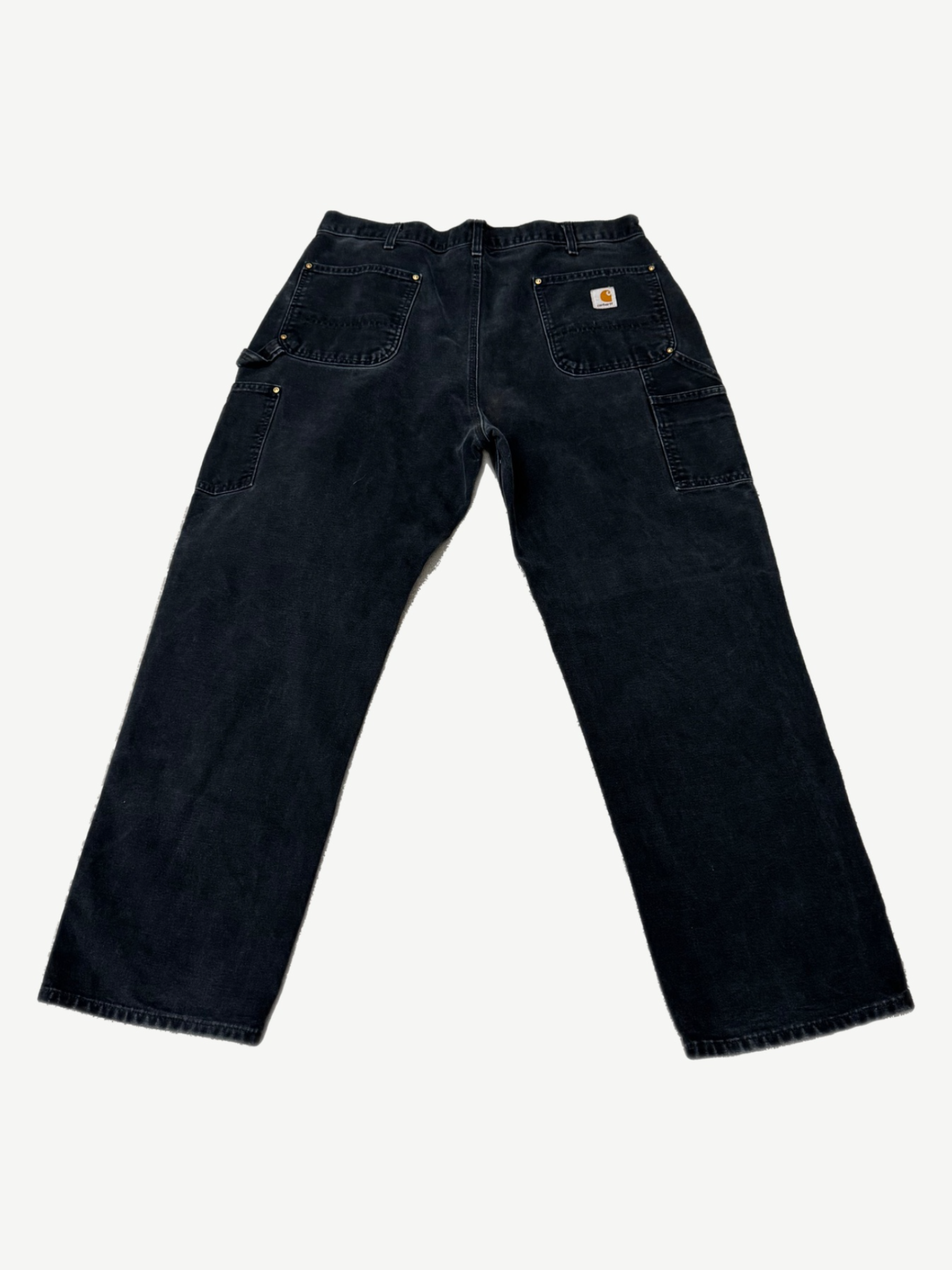 Back of vintage Carhartt black double knee carpenter pants showing Carhartt label and worn workwear fade
