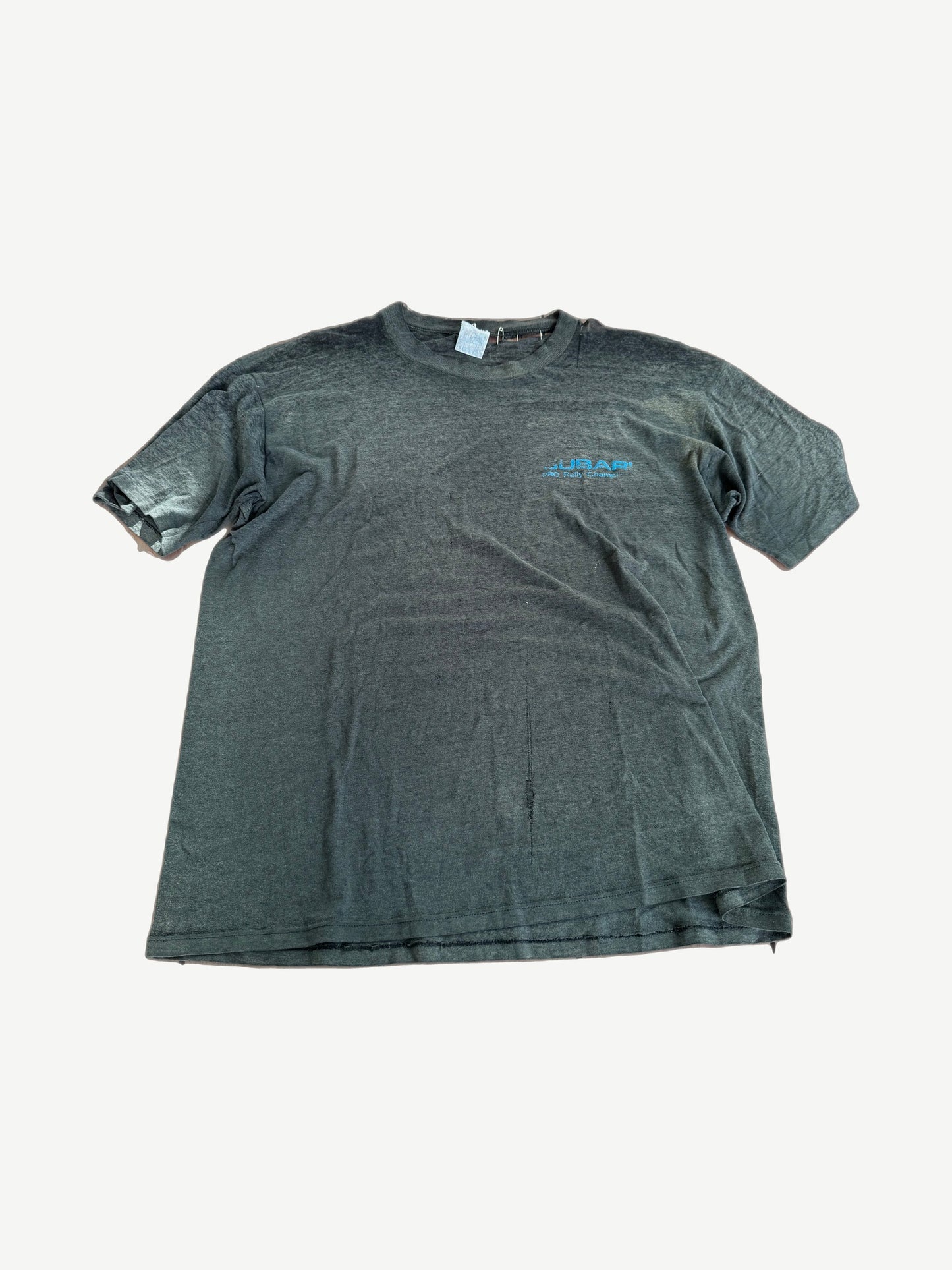 Vintage Subaru faded black tee with small blue chest logo and safety pin detail at sleeve.