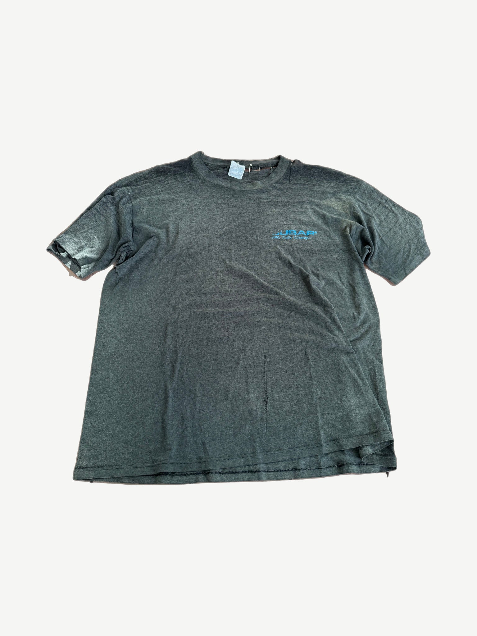 Vintage Subaru faded black tee with small blue chest logo and safety pin detail at sleeve.